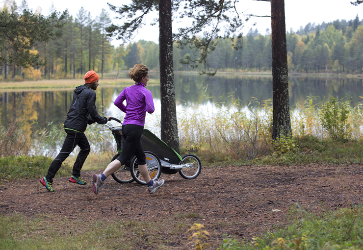 Två personer joggar invid en sjö. En av dem drar en barnvagn.
