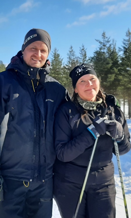 Lärarna Jesper och Marlene står tillsammans. Marlene har skidorna på sig. Bakom dem är klarblå himmel och runt dem vit snö. 