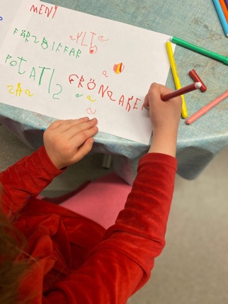 Ett barn skriver maträtter på ett A4-ark med färggranna pennor.