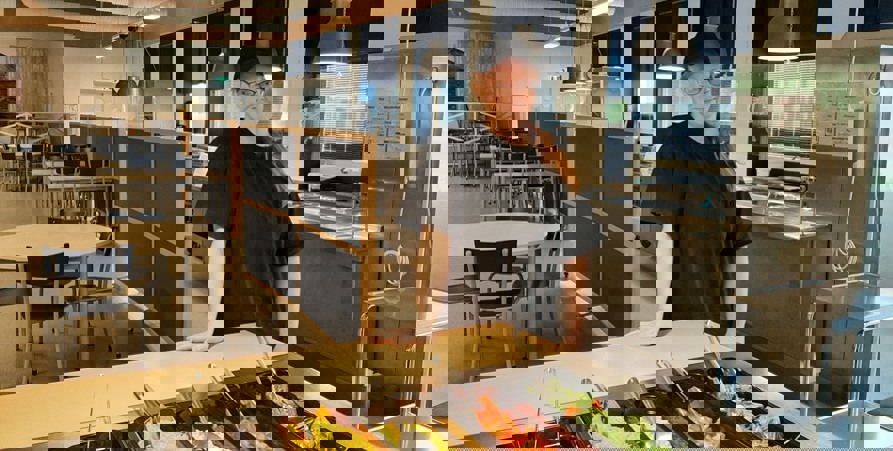 Moa-Lill med svarta kläder och en keps står med salladsbuffén framför sig i matsalen på Hembergsskolan.