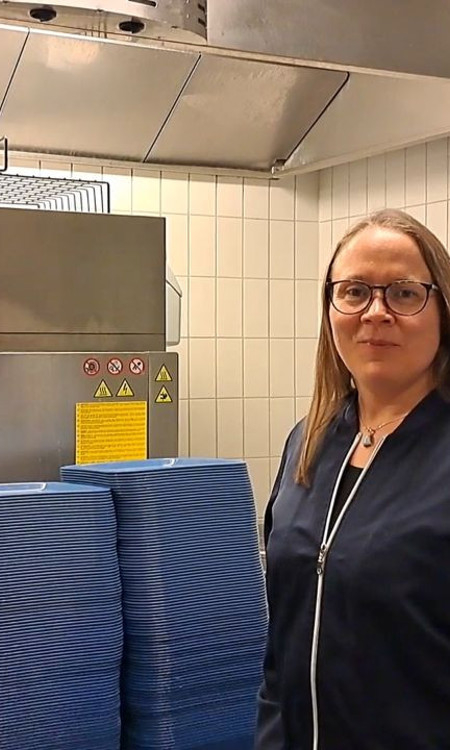 Två personer står i diskrummet. Bakom sig har de en hög stapel med blåa brickor och bakom det är diskmaskinen.