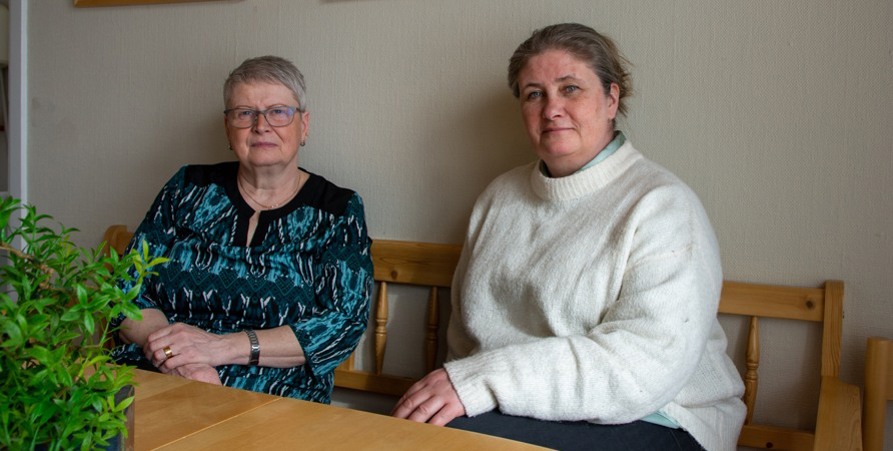 Barbro och Jenny sitter ner i en soffa. Framför sig har de ett bord med en grön växt i förgrunden. 