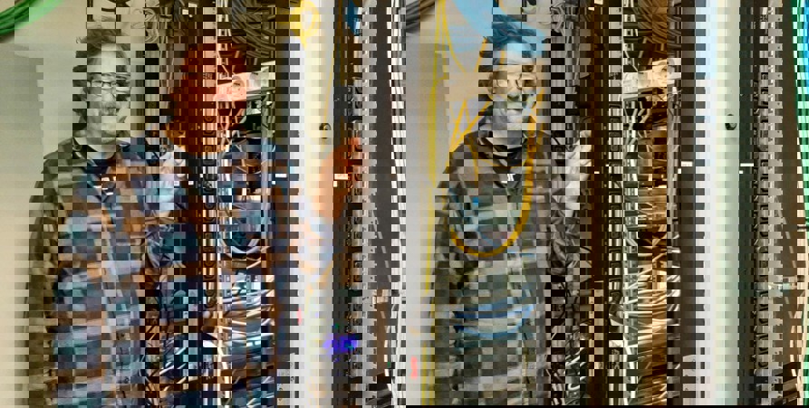 Gösta står i ett serverrum med många sladdar bredvid sig.