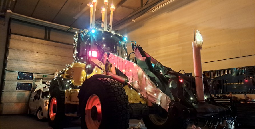 En gul traktor med många ljusslingor och på taket en luciakrona. 