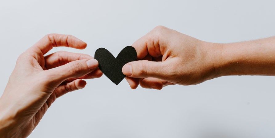 Två händer som håller ett hjärta i svart färg mellan sig. 